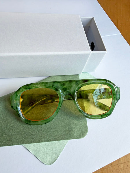 Green sunglasses with yellow lenses on a white surface